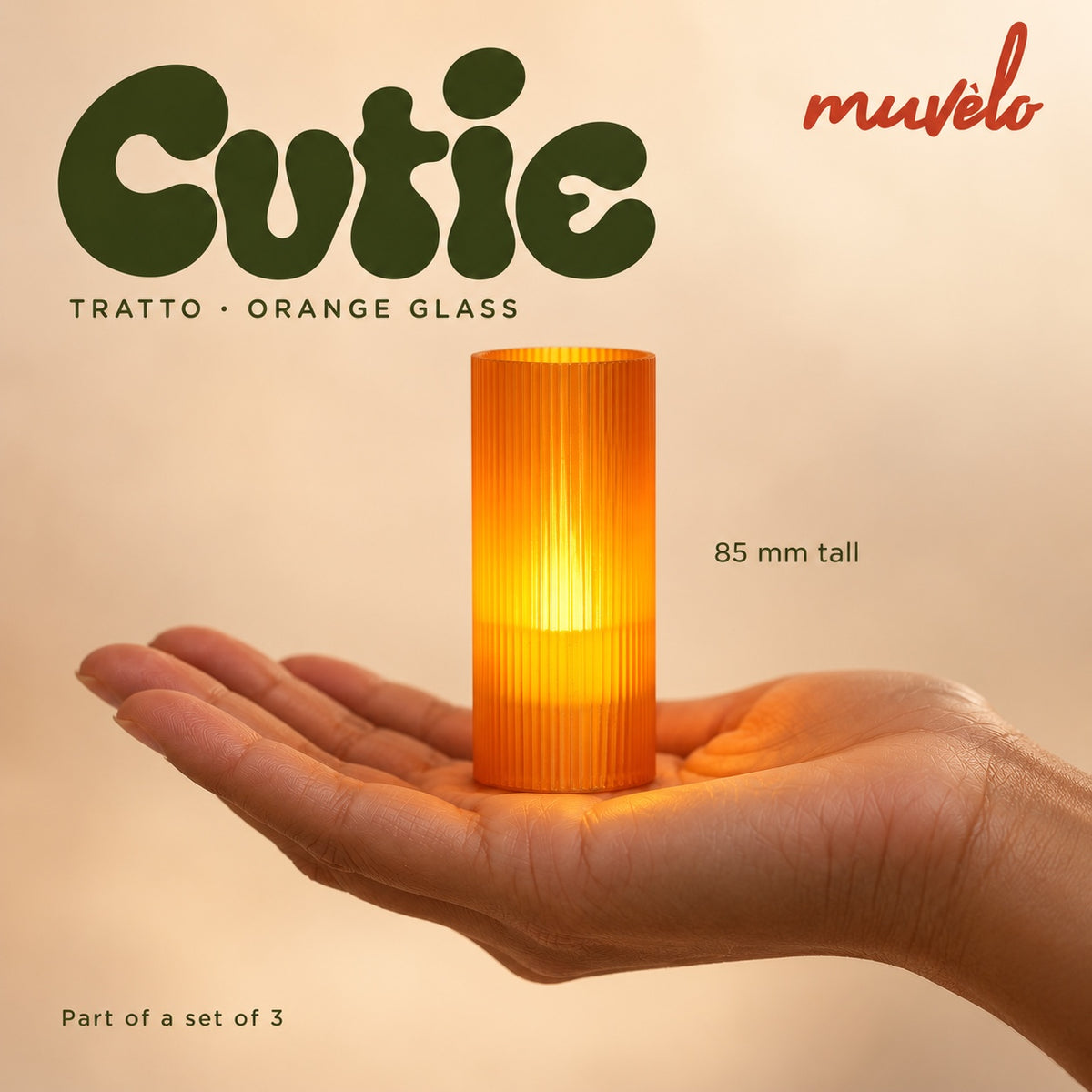 Illuminated Orange Glass Tratto Cutie resting on an adult palm, with soft retro Cutie lettering and the official Muvèlo wordmark.