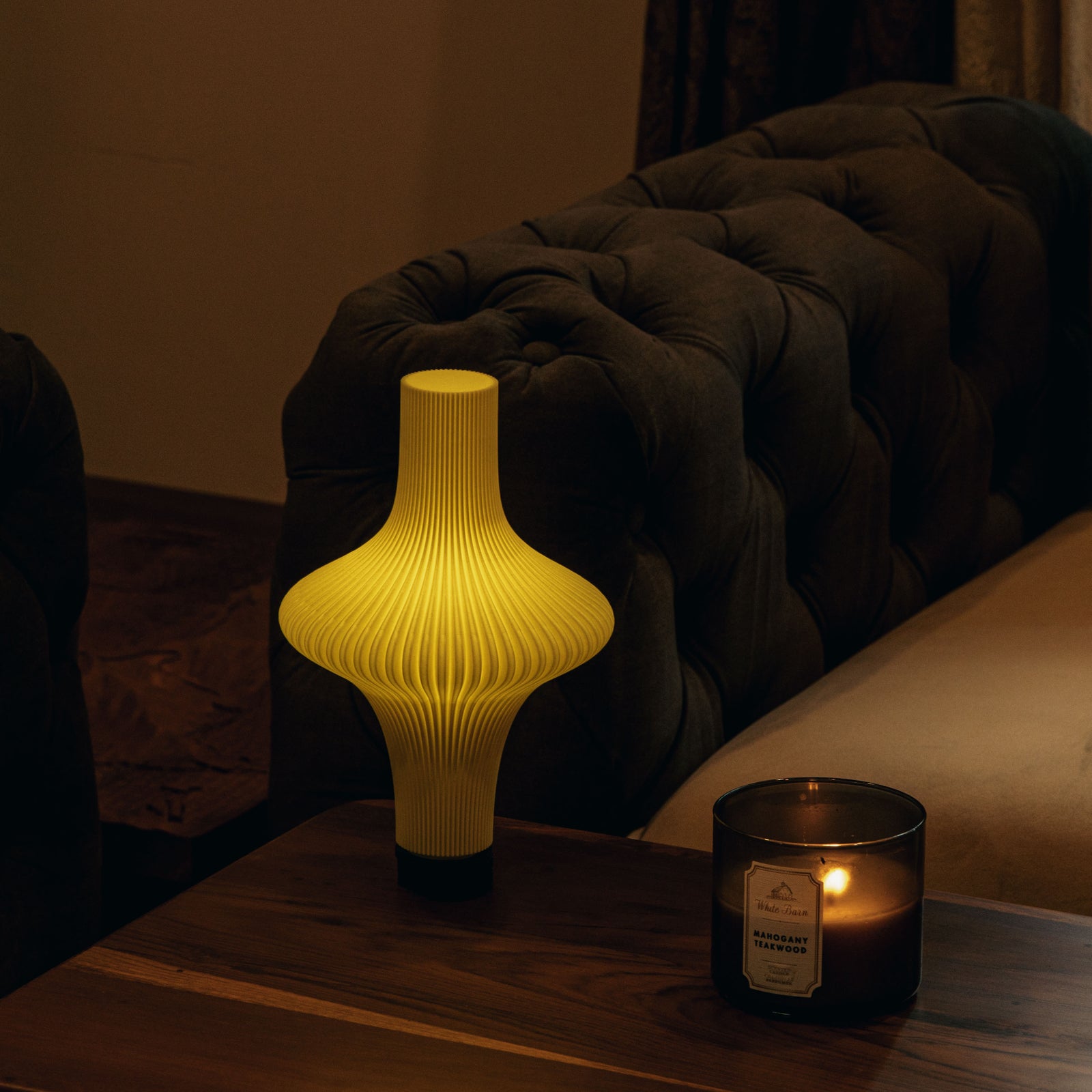 Yellow textured table lamp and candle on a wooden surface with a dark sofa in the background