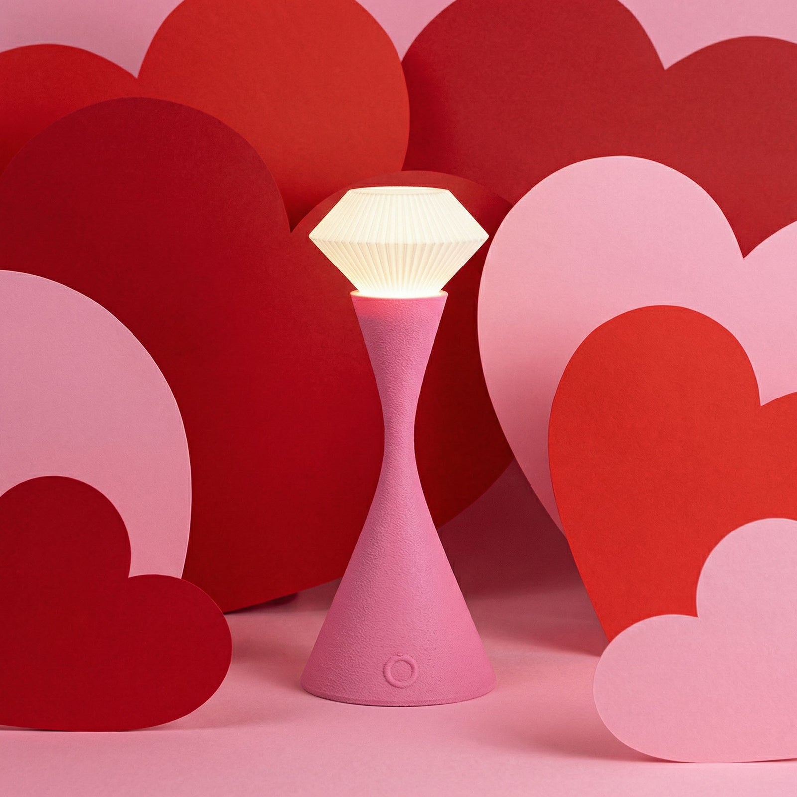Pink lamp with a white light bulb on a pink background with red heart shapes