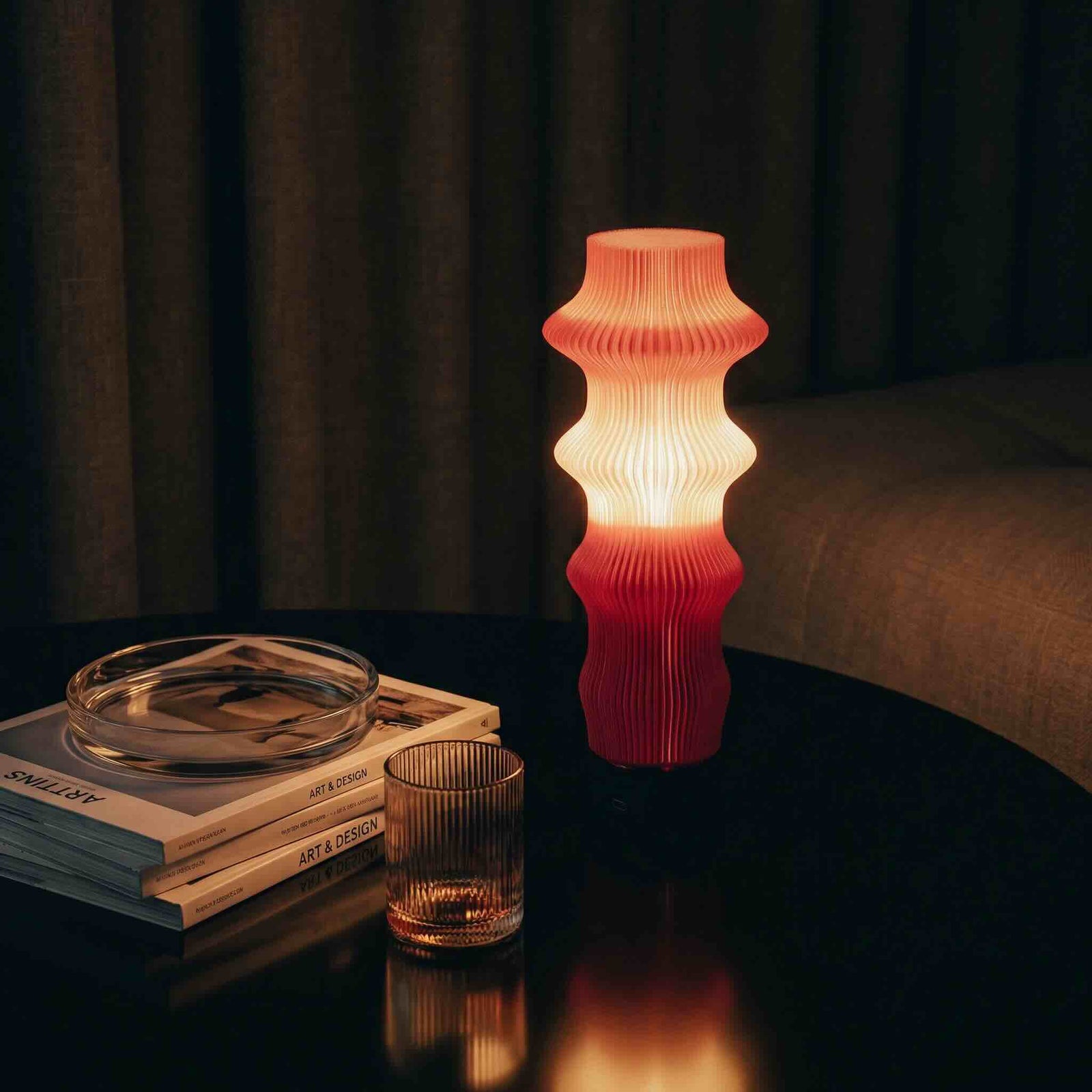 Decorative table lamp with a ribbed design on a dark surface with books and glasses.