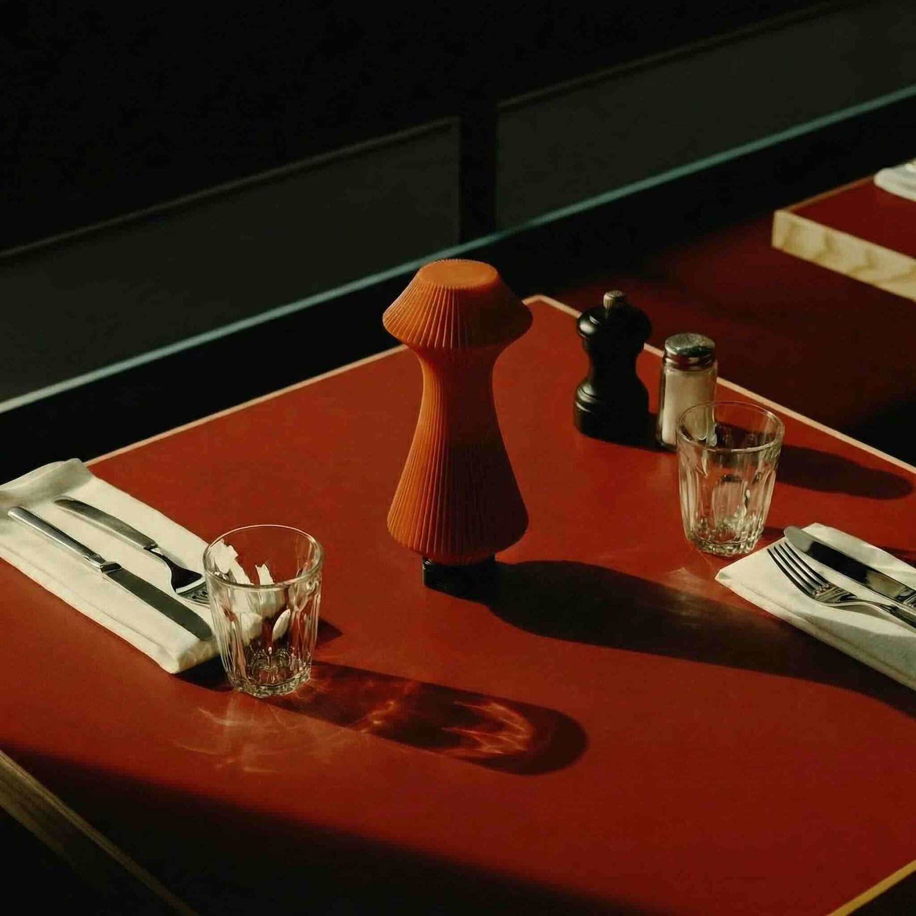 Dining setup with cutlery, glasses, and salt and pepper shakers on a red table.
