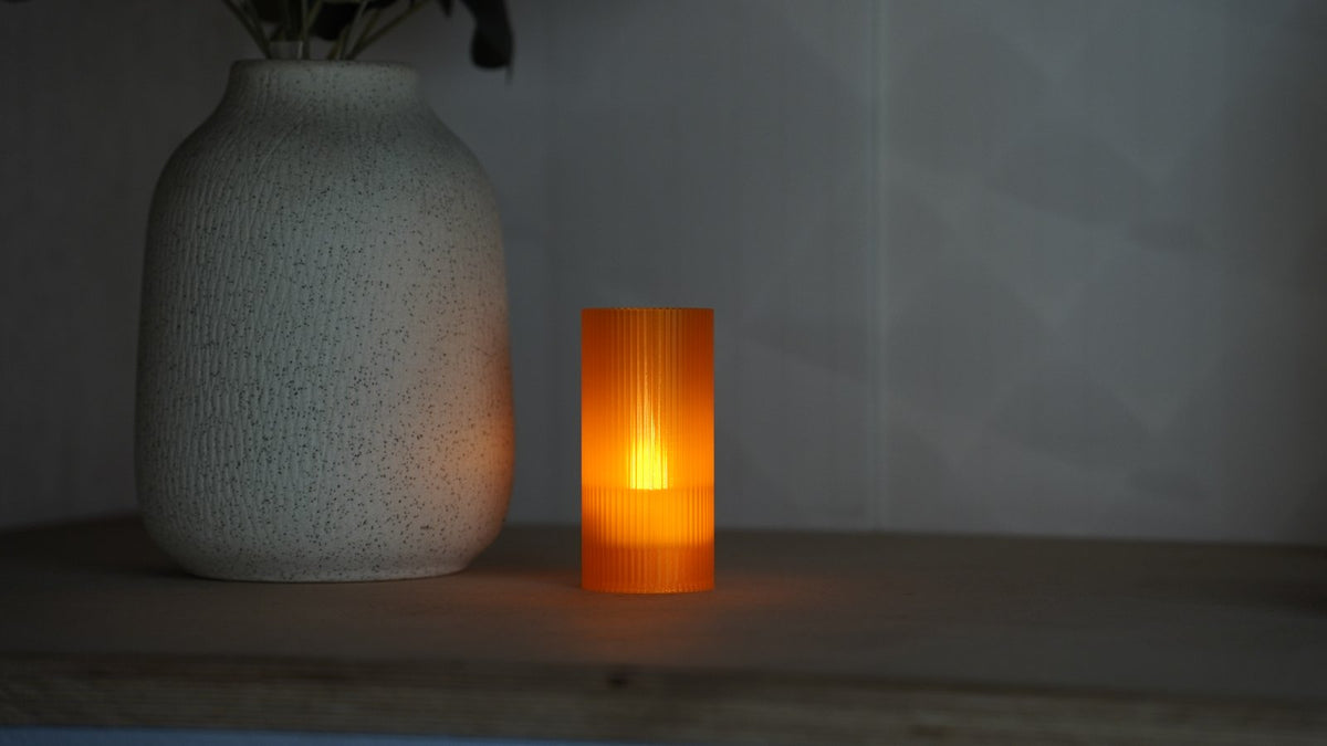 Original photograph of the Orange Glass Tratto Cutie lamp glowing on a shelf beside a textured vase.
