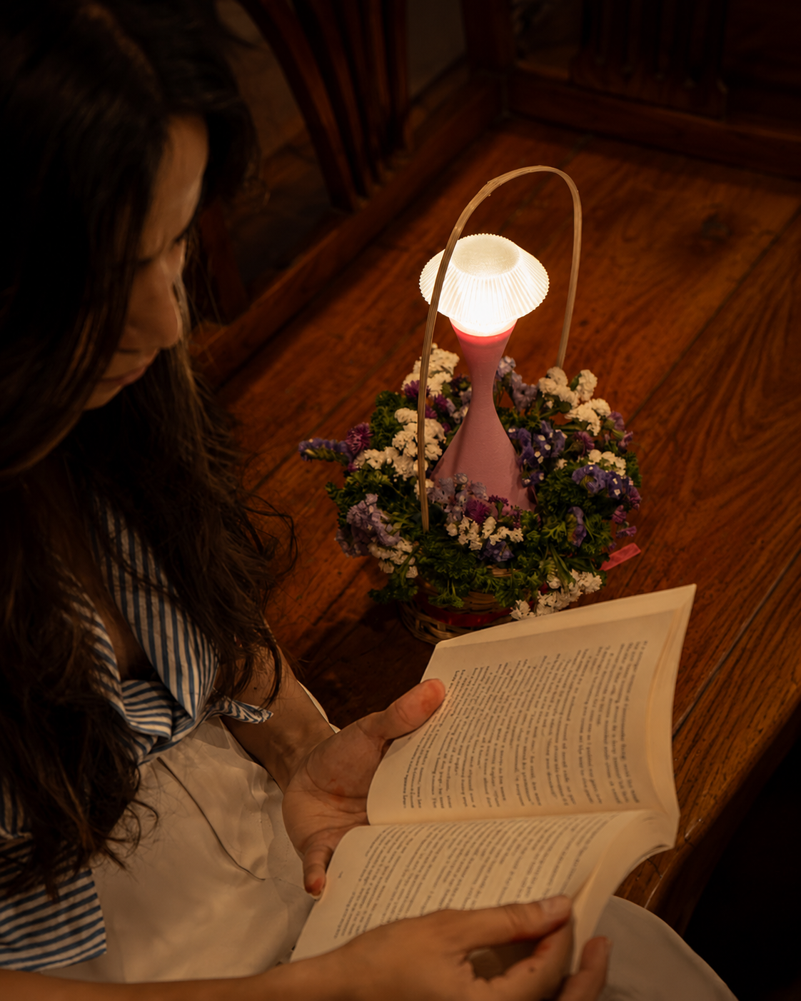 Vela Blush Pink touch control rechargeable table lamp glowing beside flowers and an open book