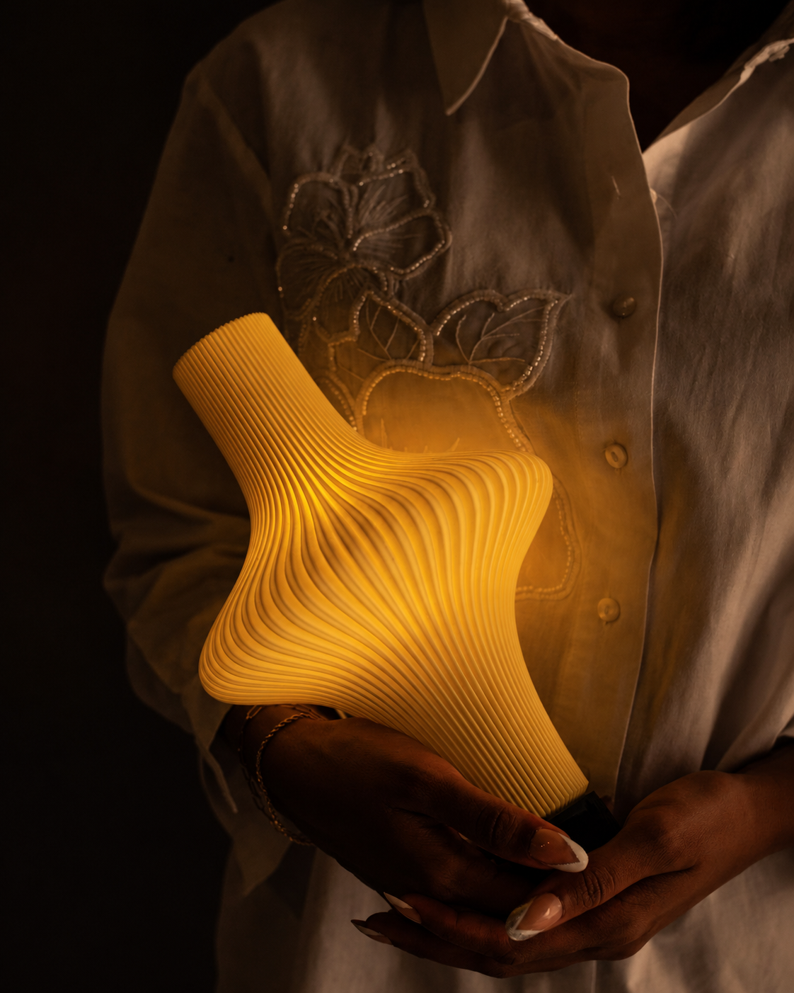 Muvèlo sculptural rechargeable portable table lamp held in hand with a warm ambient glow