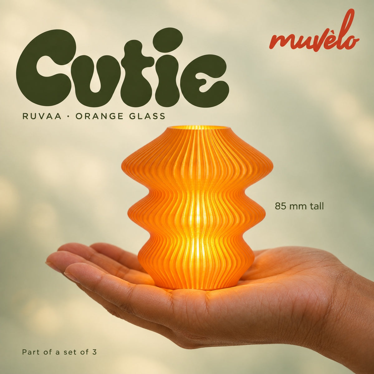 Illuminated Orange Glass Ruvaa Cutie resting on an adult palm, with soft retro Cutie lettering and the official Muvèlo wordmark.