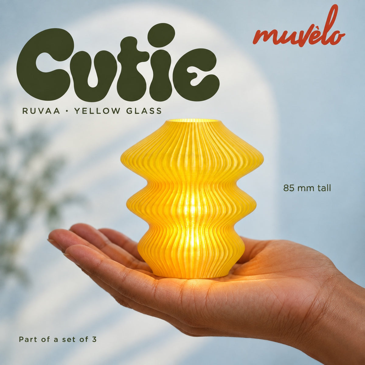 Illuminated Yellow Glass Ruvaa Cutie resting on an adult palm, with soft retro Cutie lettering and the official Muvèlo wordmark.