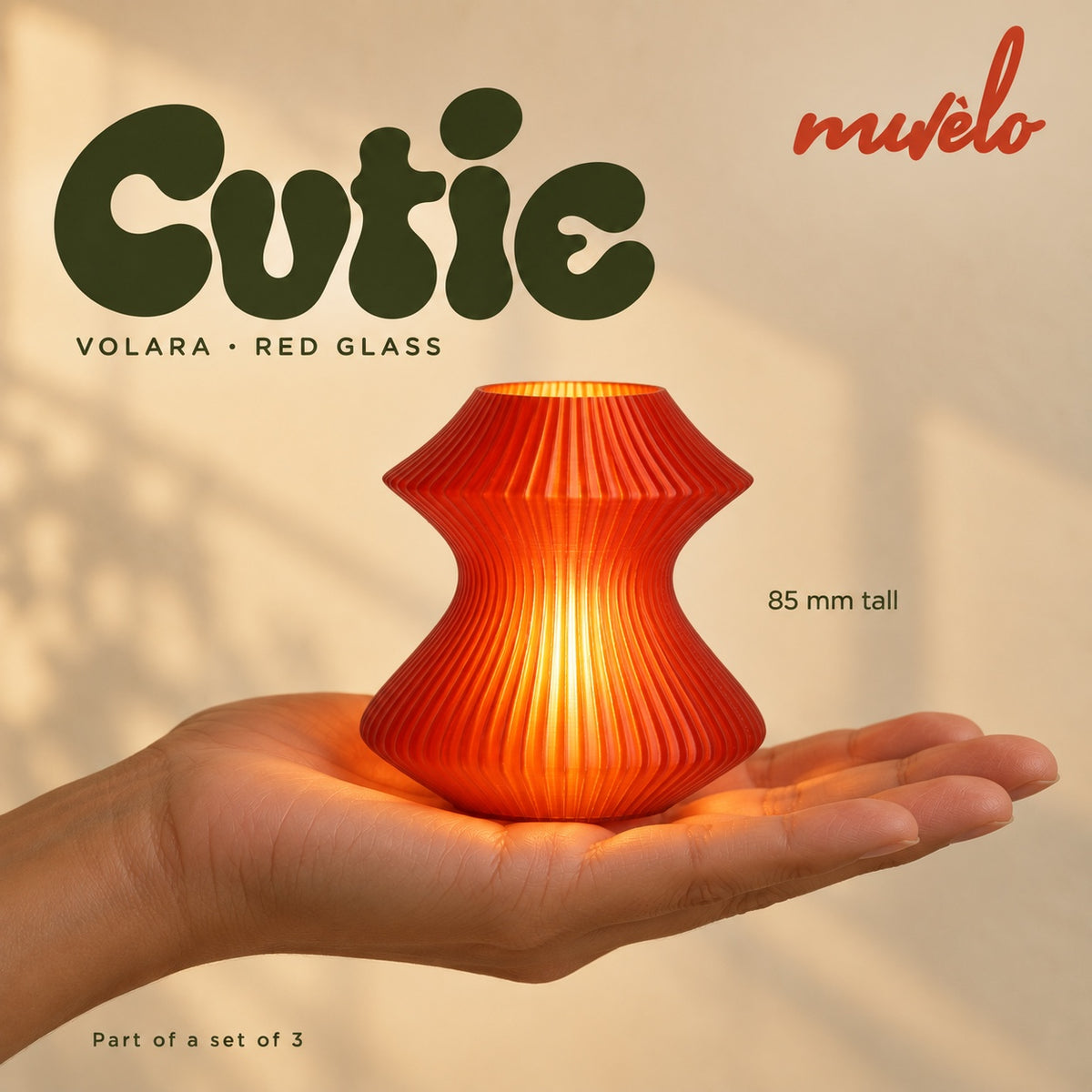 Illuminated Red Glass Volara Cutie resting on an adult palm, with soft retro Cutie lettering and the official Muvèlo wordmark.