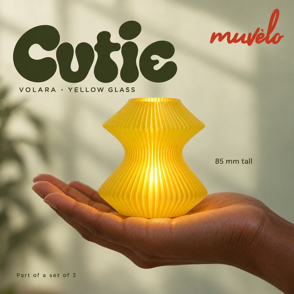 Illuminated Yellow Glass Volara Cutie resting on an adult palm, with soft retro Cutie lettering and the official Muvèlo wordmark.