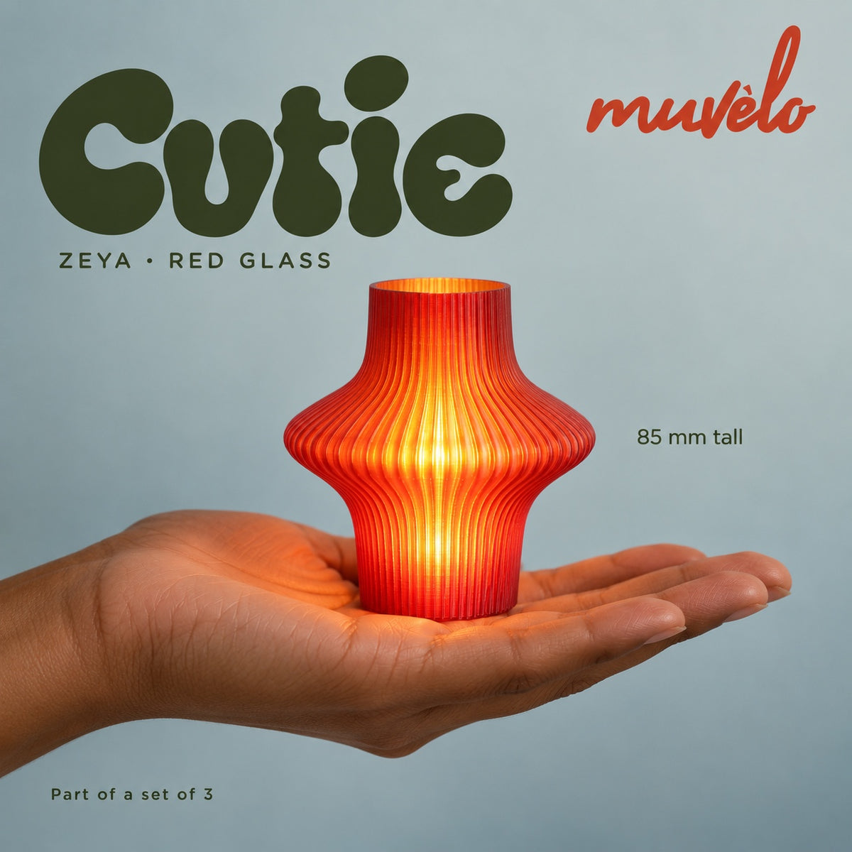 Illuminated Red Glass Zeya Cutie resting on an adult palm, with soft retro Cutie lettering and the official Muvèlo wordmark.