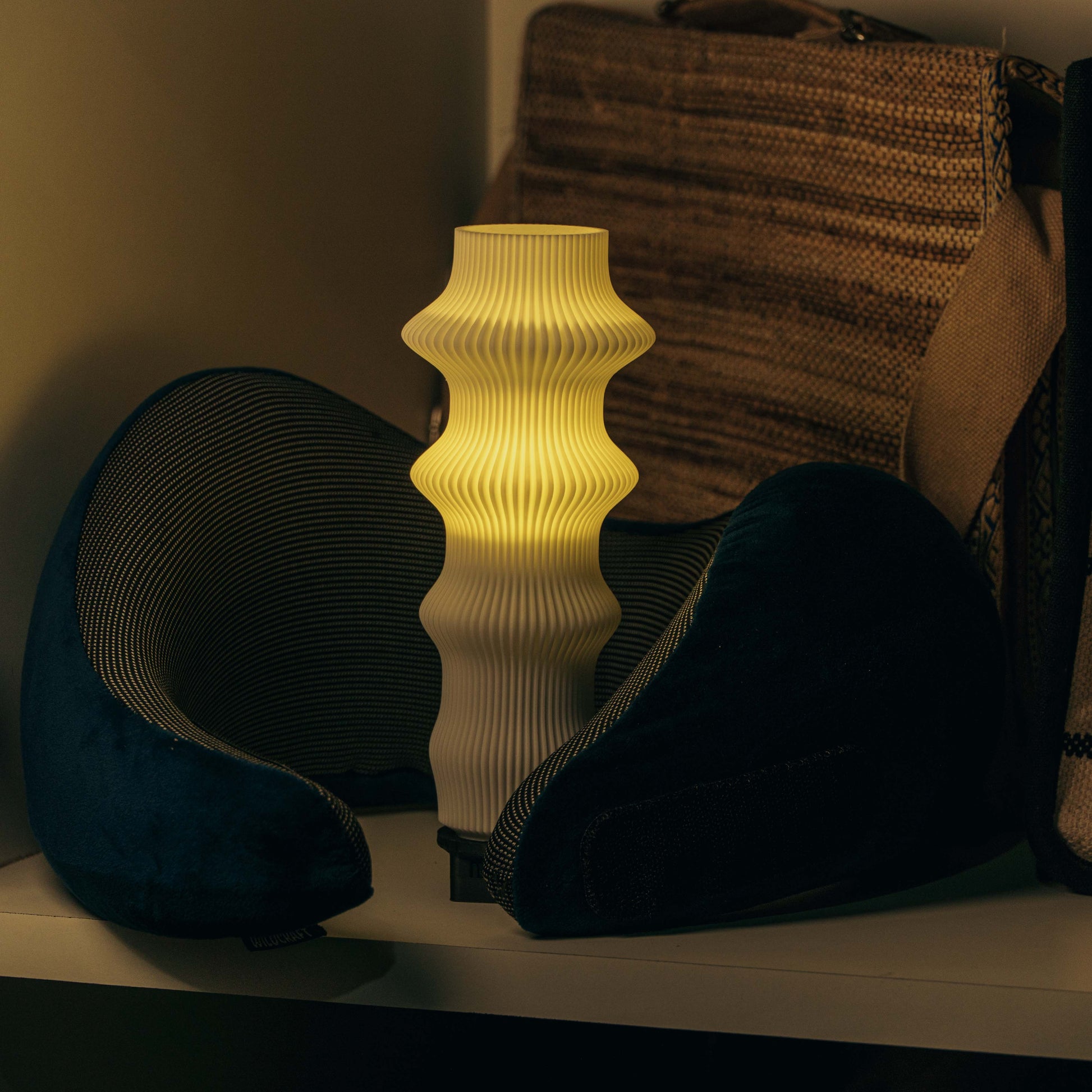 Decorative lamp with ribbed texture on a shelf with pillows in the background