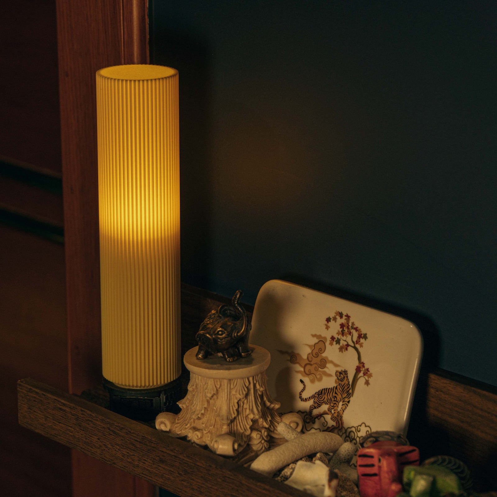 Yellow ribbed lamp on a shelf with decorative items in a dimly lit room