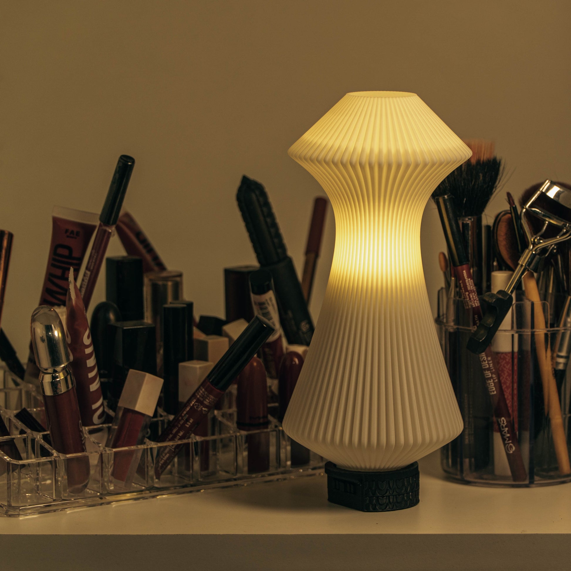 Decorative lamp with ribbed design on a surface with makeup brushes and products in the background.