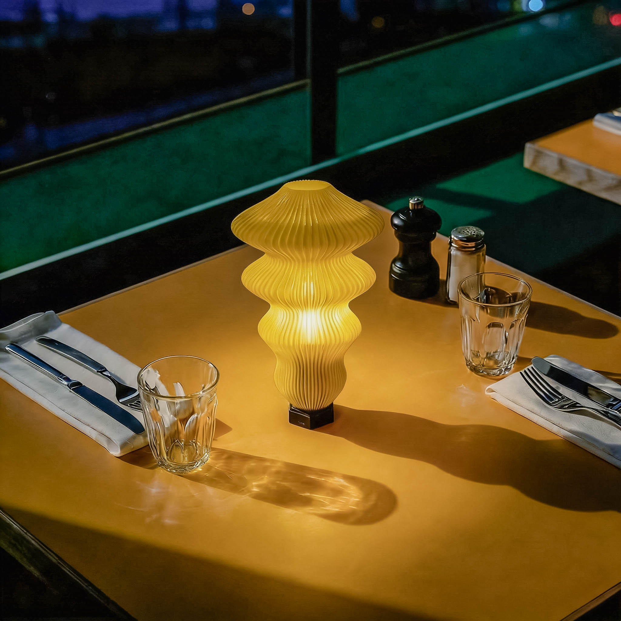 Yellow table lamp on a wooden table with glasses and cutlery, blurred background