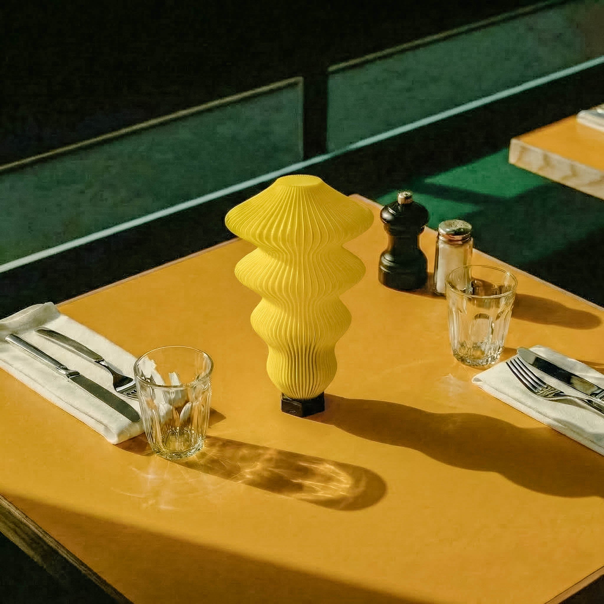 Yellow decorative vase on a table with cutlery and glasses Yellow table lamp on a wooden table with glasses and cutlery, blurred background