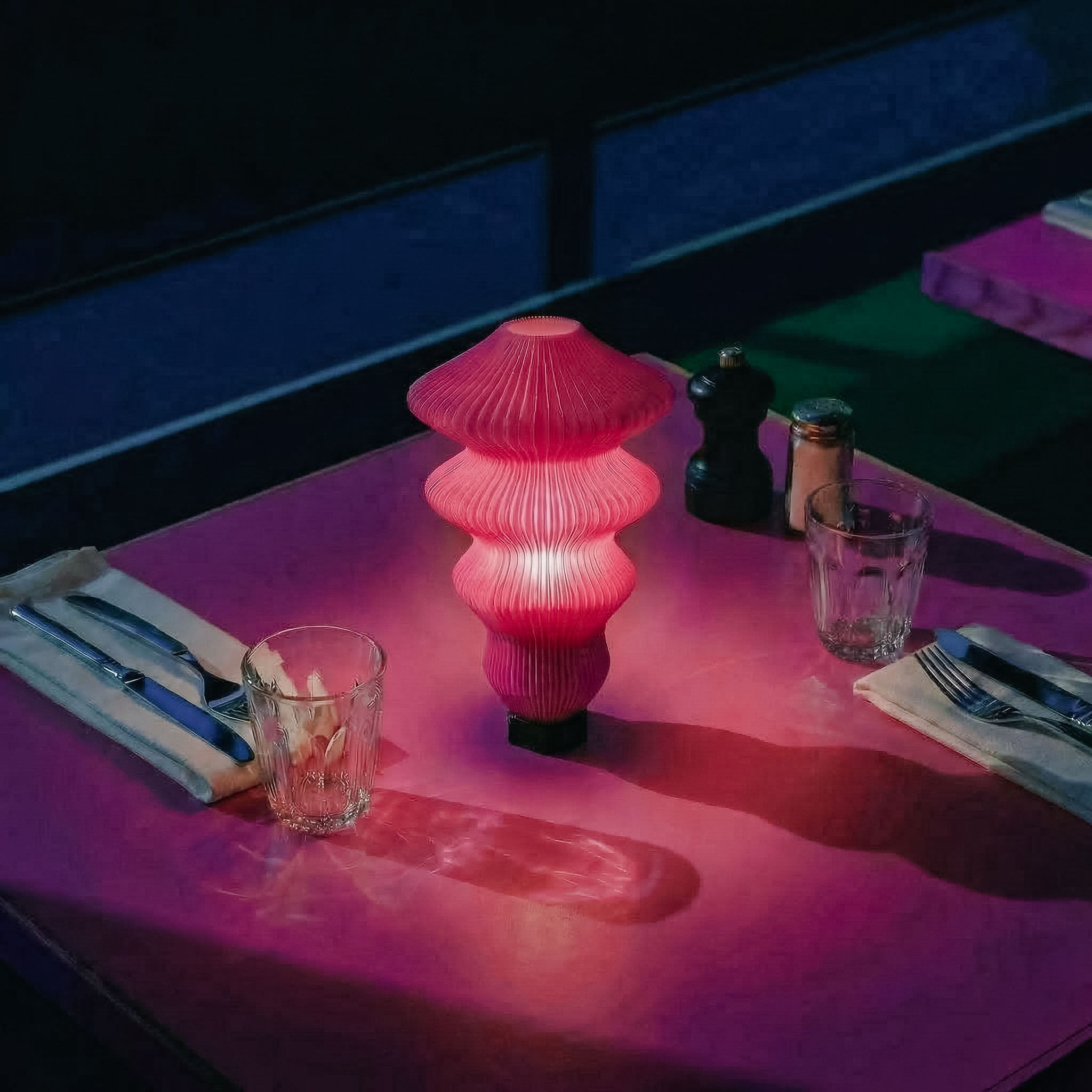 Pink table lamp on a dining table with cutlery and glasses in a dimly lit setting