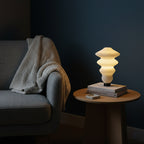 Modern lamp on a side table next to a gray sofa with a blanket draped over it.