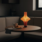 Table with a lit lamp, cup, and croissant in a dimly lit room.