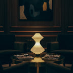 Modern lamp on a table in a dimly lit room with chairs and a painting.