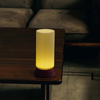 Cylindrical lamp with ribbed design on a wooden table in a dimly lit room.