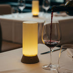 Wine being poured into a glass on a table with a lit lamp and cutlery.