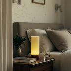 Lamp on a nightstand next to a sofa with cushions in a dimly lit room.