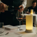 Wine being poured into a glass on a table with a waiter and restaurant setting.