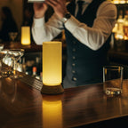 Barista preparing a drink at a bar with a lit lamp on the counter.
