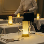 Waiter setting tables in a dimly lit restaurant with candles and white tablecloths.