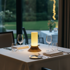 Dining table set with wine glasses, a lamp, and cutlery with a blurred outdoor background.