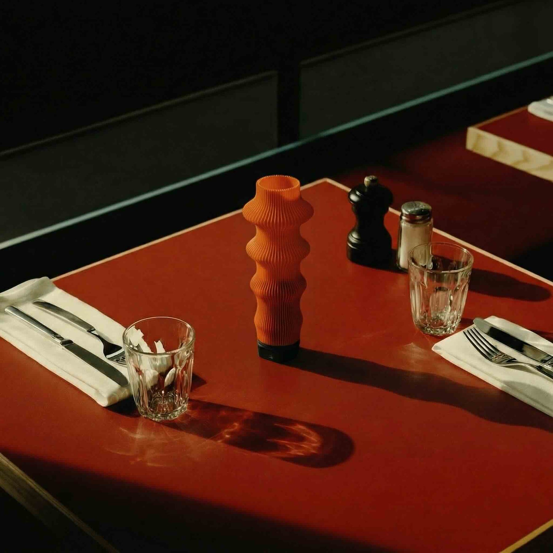 Dining table setup with cutlery, glasses, and a red vase on a dark background