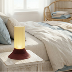 Table lamp on a nightstand next to a bed with a wicker chair in the background