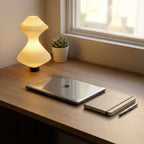 Laptop on a wooden desk with a lamp, notebook, and pen in a home office setting.