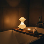 Relaxing bath scene with a lit candle and decorative lamp in a dimly lit bathroom.