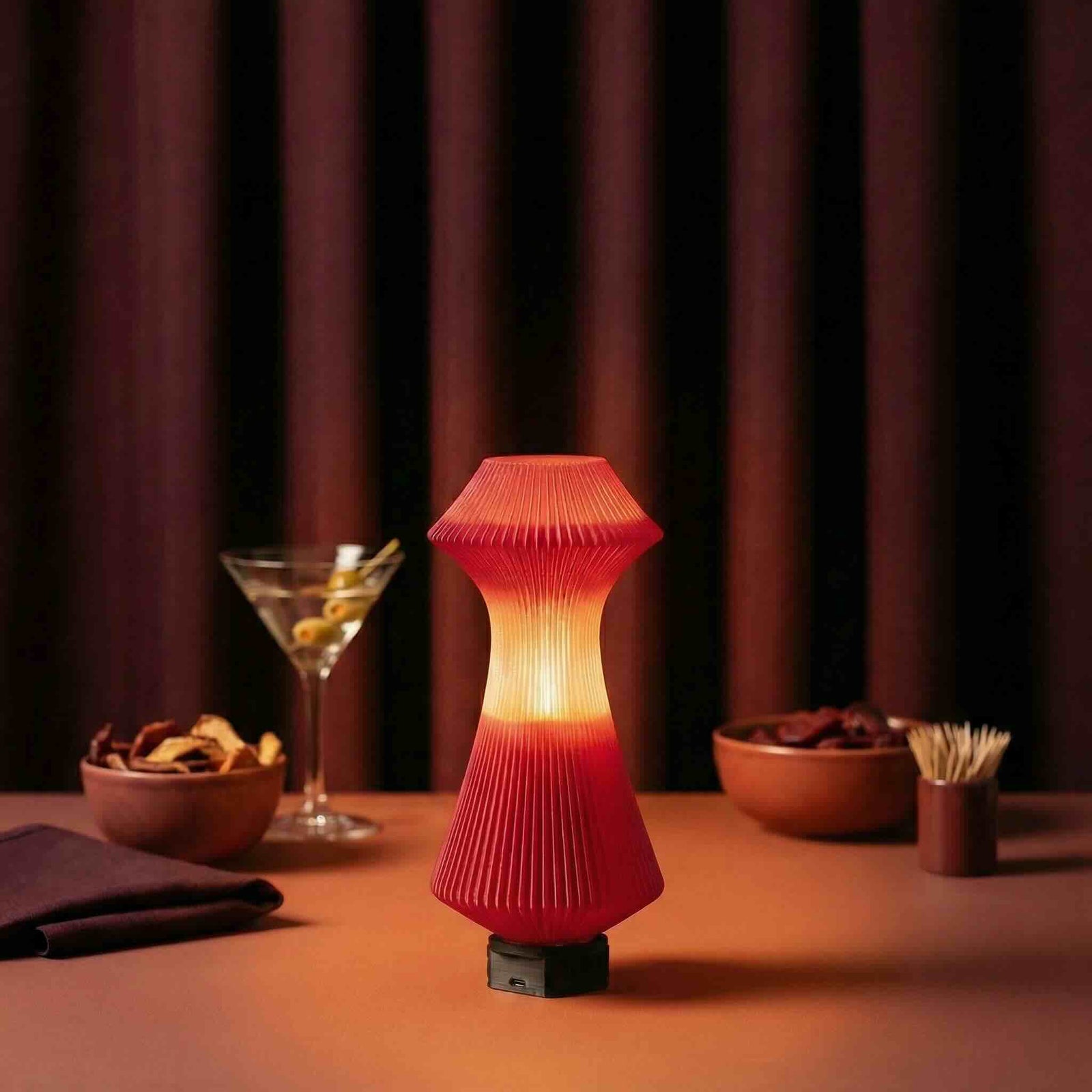 Red textured table lamp on a table with snacks and a cocktail in a dimly lit room.