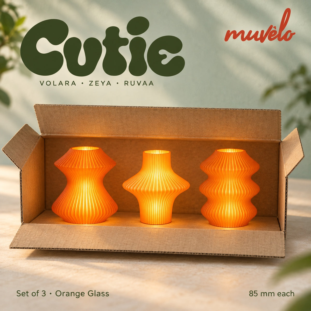 Three illuminated Orange Glass Cutie lamps — Volara, Zeya, Ruvaa — displayed together in an open plain cardboard box.