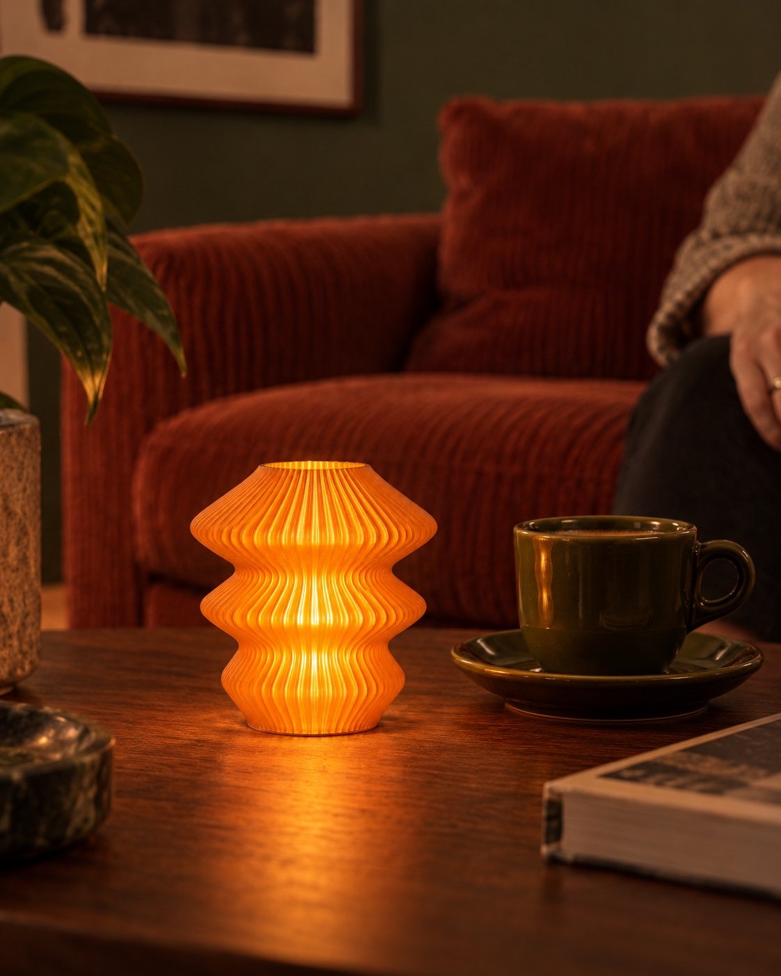 Orange Glass Ruvaa Cutie lamp glowing on a wooden coffee table beside a cup, with a rust-coloured sofa behind.