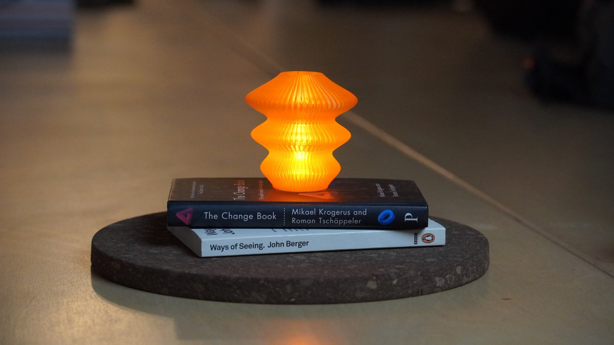 Original photograph of the Orange Glass Ruvaa Cutie lamp glowing on stacked books and a round display mat.