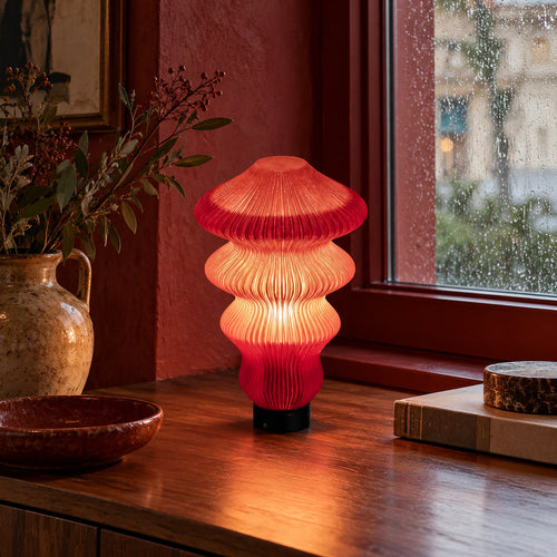 Muvèlo Ruvaa Max Red Glass table lamp glowing beside a rain-covered window