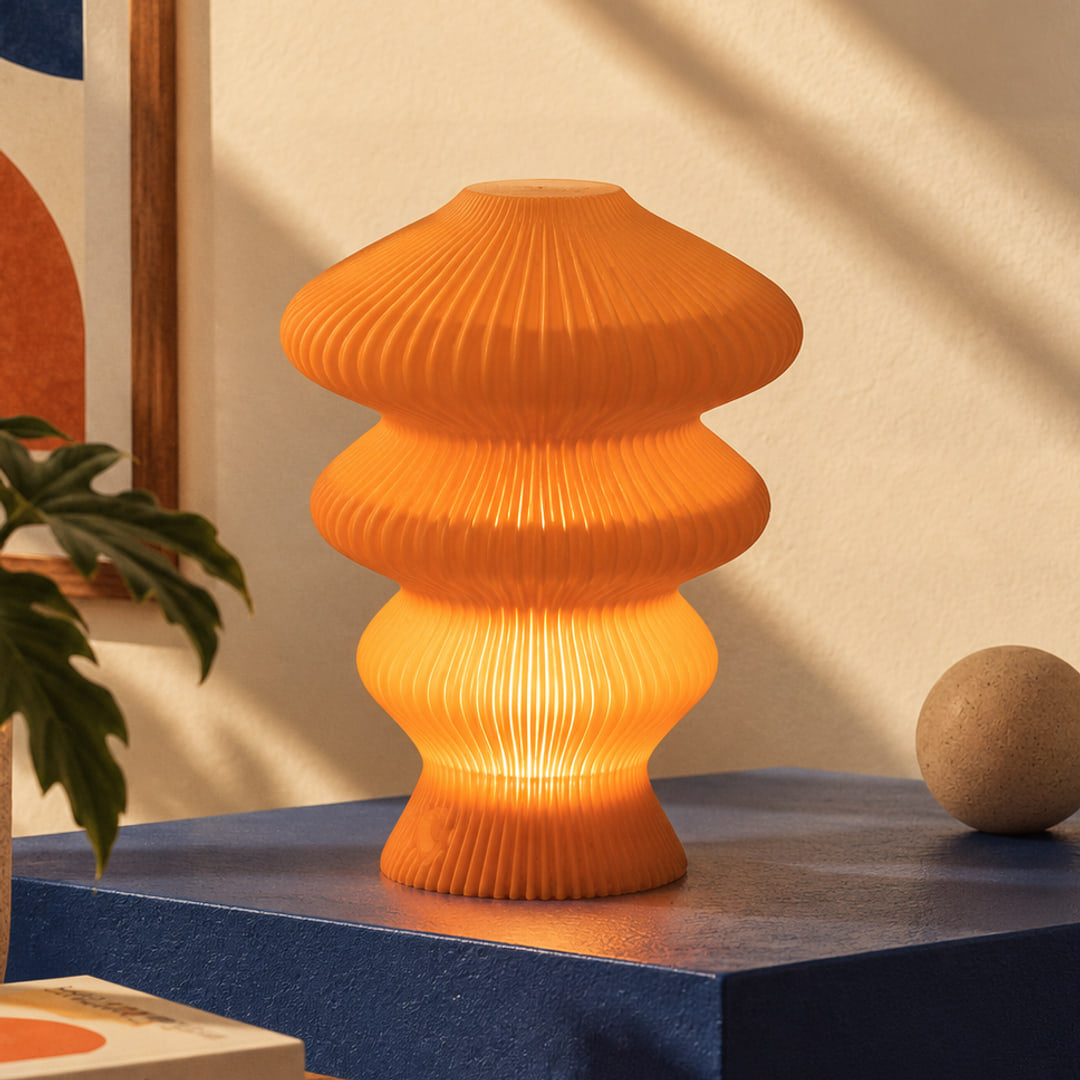 Muvèlo Ruvaa Mono Orange table lamp glowing on a blue display plinth in a retro interior