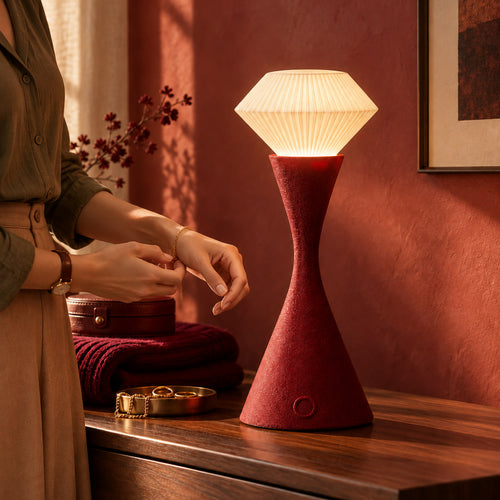 Muvèlo Vela Maroon table lamp on a dressing table beside hands fastening a bracelet