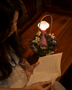 Vela Blush Pink touch control rechargeable table lamp glowing beside flowers and an open book