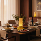 Dining table set with plates of food, wine glasses, and a lamp in a cozy room.